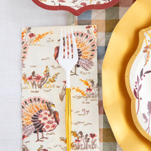 Load image into Gallery viewer, The Amber Harvest Table Setting by Sophistiplate features a white fork with a gold handle resting on a napkin adorned with colorful turkeys, accompanied by designer disposable plates and a patterned plate atop a plaid tablecloth, creating an inviting autumn tablescape.