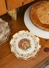 Load image into Gallery viewer, A decorative Turkey & Gourds: Thanksgiving Table for 16 setting featuring a turkey illustration on a disposable party plate, placed on a wooden surface next to a whole pie and a glass filled with gold cutlery.