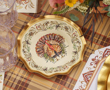 Load image into Gallery viewer, The Sophistiplate LLC Turkey & Gourds Table Setting Bundle features a decorative plate with a detailed turkey illustration at the center and a floral border, elegantly arranged on a plaid tablecloth alongside glassware and cutlery—a perfect example of designer disposable plates that blend festive style with convenience for any holiday gathering.