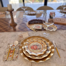 Load image into Gallery viewer, Sophistiplate Turkey & Gourds Table Setting featuring a gold-rimmed designer paper plate with a pumpkin illustration, gold-handled flatware, and a matching patterned napkin on a marble table.