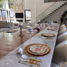 Load image into Gallery viewer, A Turkey & Gourds: Thanksgiving Table for 16 set on a long marble table with pumpkin-illustrated paper plates, gold chargers, patterned napkins, white cutlery, and wine glasses.