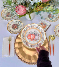 Load image into Gallery viewer, A hand sets the Sophistiplate Turkey &amp; Gourds Table Setting, featuring a designer paper plate, at a fall-themed table with matching napkin, cutlery, and a floral and succulent centerpiece.
