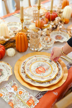 Load image into Gallery viewer, A hand arranges the Sophistiplate Turkey &amp; Gourds Table Setting on an autumn table with Thanksgiving tableware—gold-rimmed plates, candles, glasses, mini pumpkins—plus a fall-patterned cloth and napkin.
